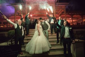 Bride and groom share a kiss surrounded by guests holding sparklers on wedding venue steps at night.