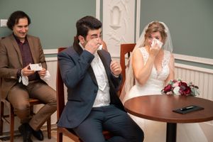Bride and groom wiping tears during emotional wedding ceremony indoors.