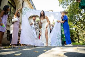 Bride and groom walk through decorative banner at outdoor wedding celebration.