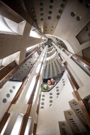 Couple smiling inside a spiral tower staircase with geometric architecture, viewed from below at Sagrada Familia.