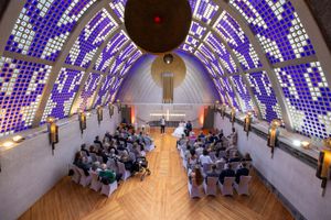 Elegant chapel ceremony with purple stained glass ceiling, wooden floors, and guests seated in rows facing the altar.