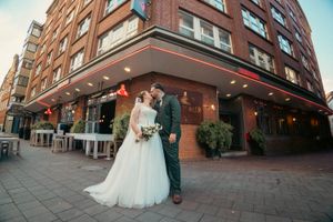 Bride and groom share a romantic kiss outside a brick building on their wedding day.