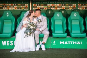 Bride and groom sharing a kiss on Werder Bremen stadium bench seats during their wedding photo shoot.