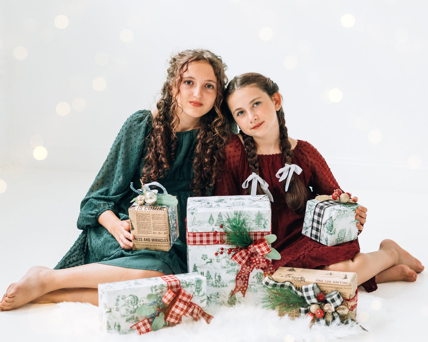 Two girls in red and green holiday dresses pose with Christmas gifts for festive Holiday Minis photo session.