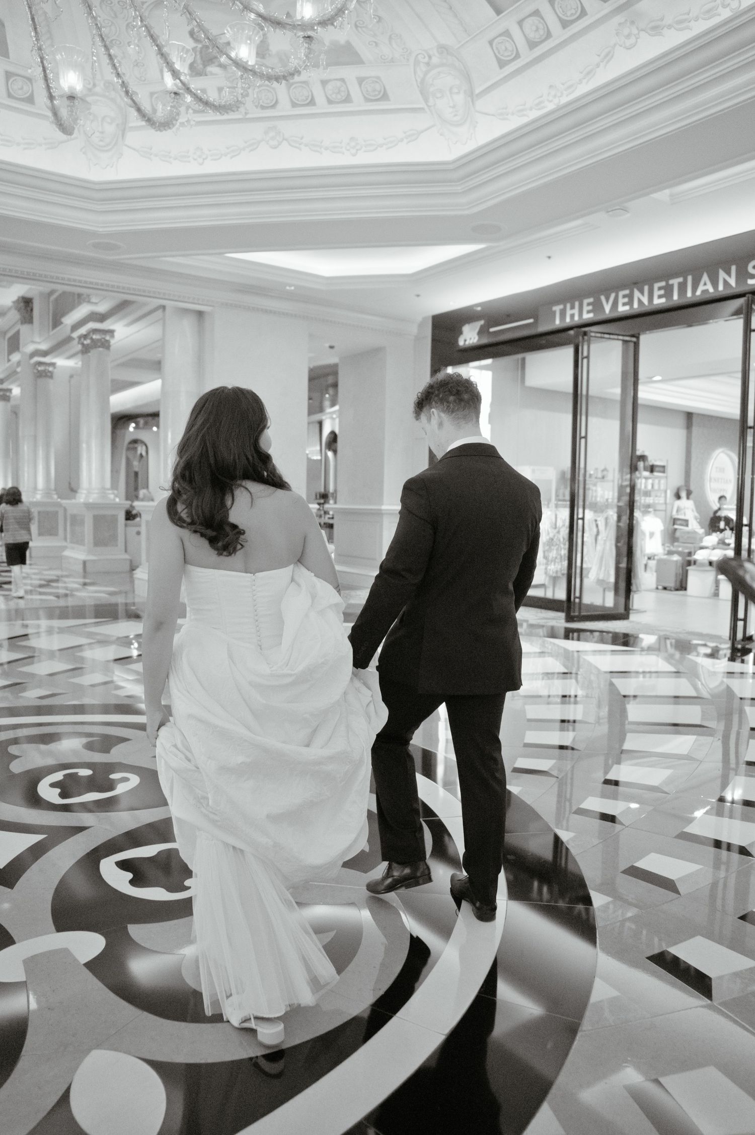 Bride and groom walking hand in hand through The Venetian Las Vegas in black and white wedding photo.