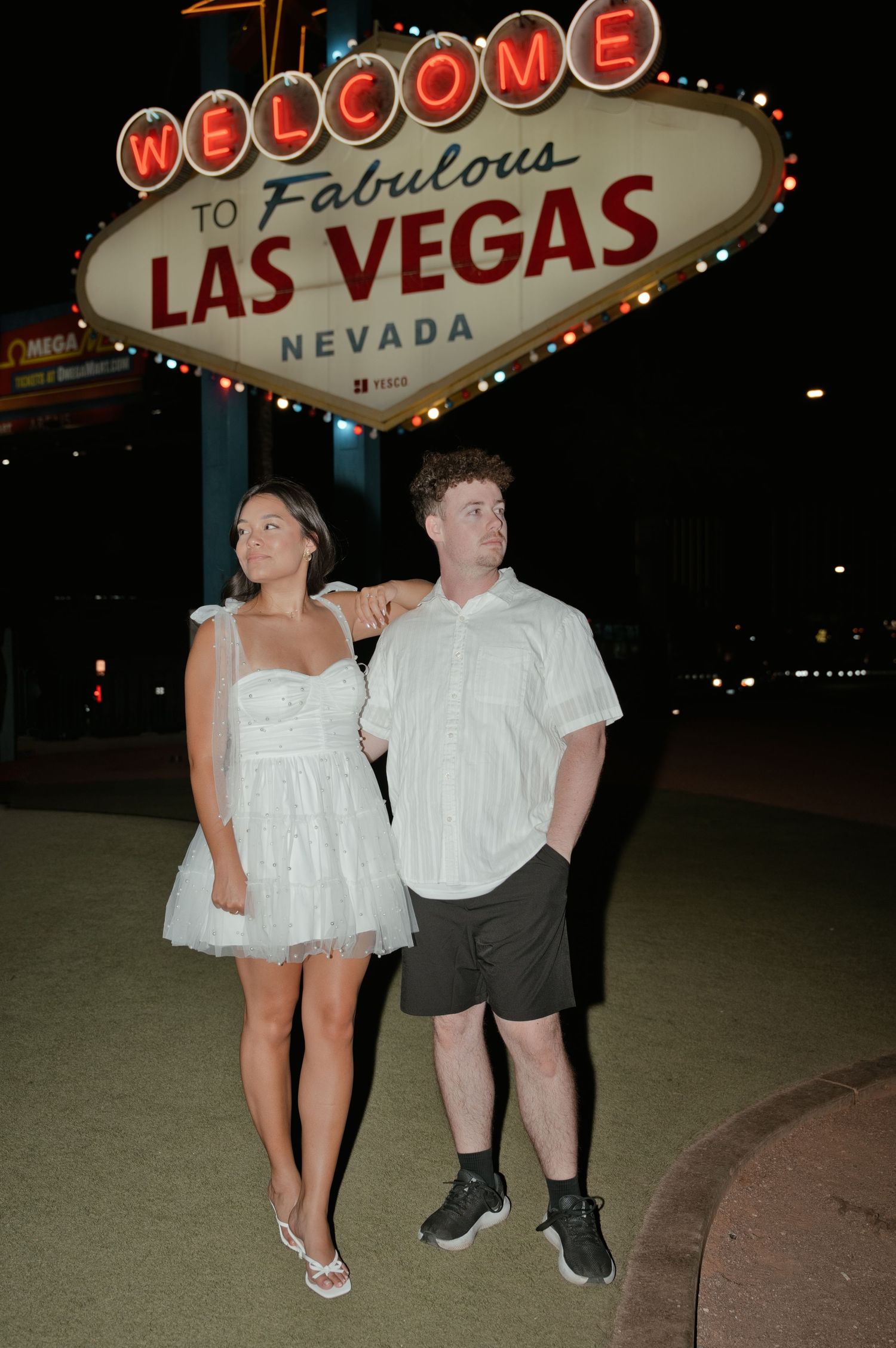 Couple in white outfits posing in front of the iconic Welcome to Fabulous Las Vegas Nevada sign at night.