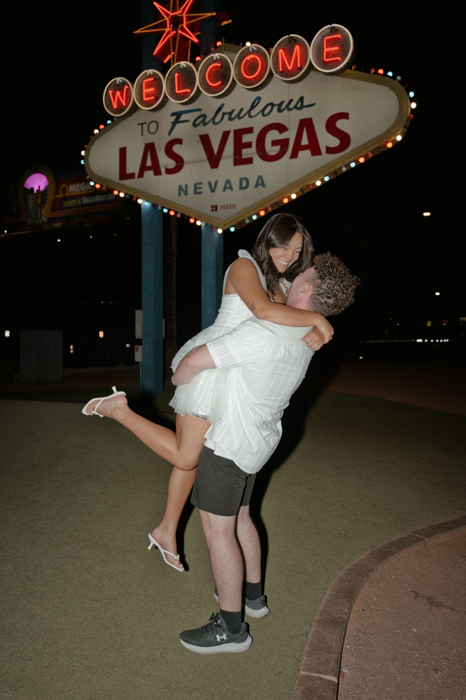 Couple embracing in front of the iconic Welcome to Fabulous Las Vegas Nevada sign at night.