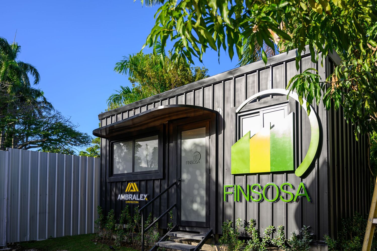 FINSOSA and AMBRALEX branded dark container office building surrounded by tropical palm trees.