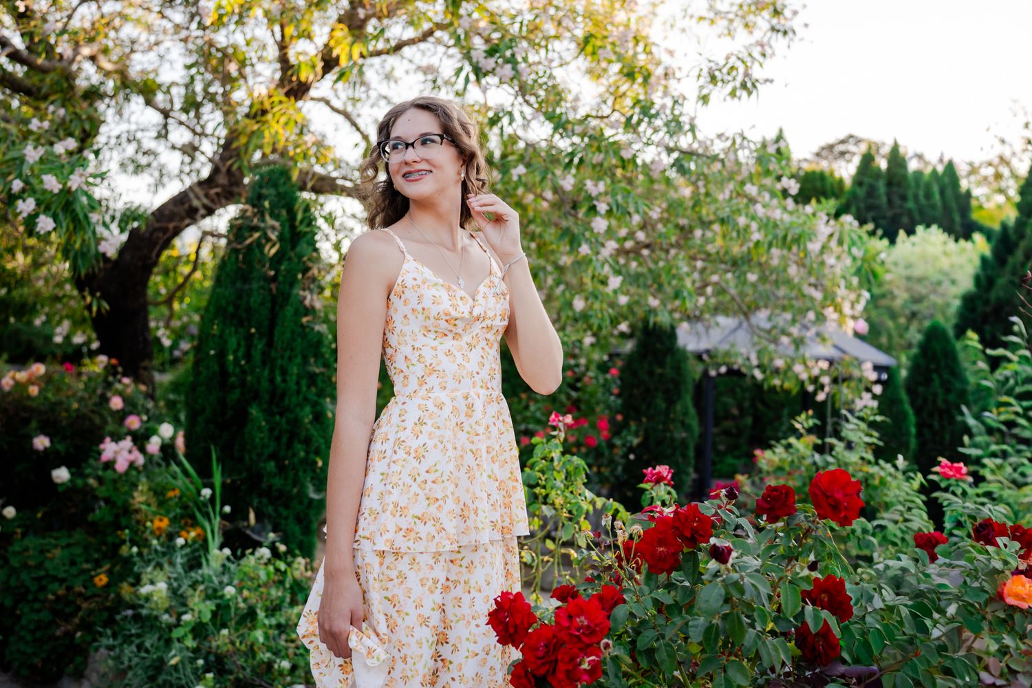 Senior portrait of a young lady by red roses and trees