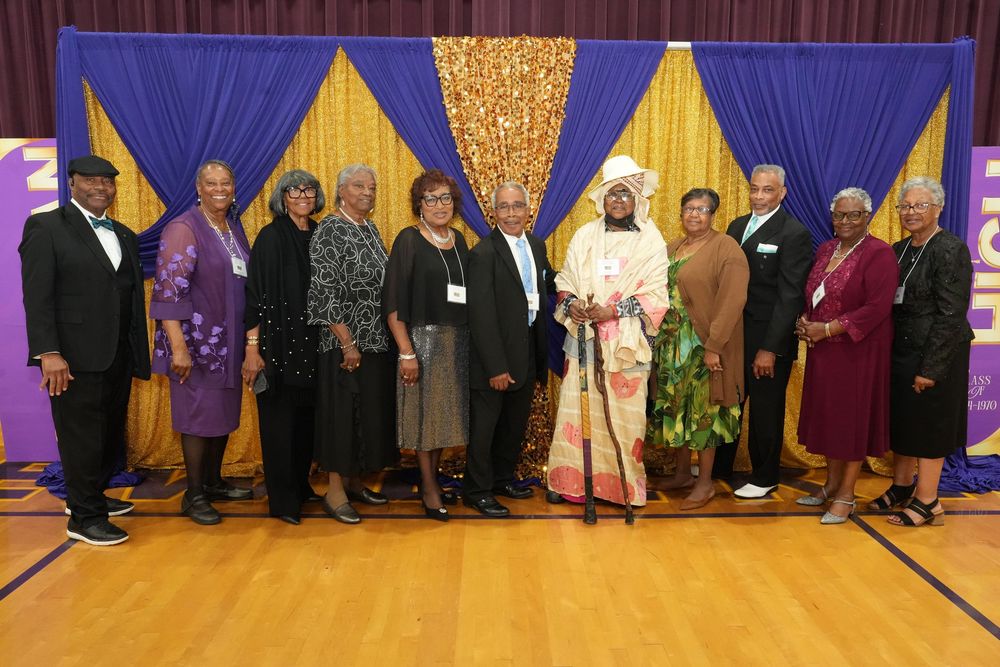 A group of ten people pose together in front of gold and purple decorative draping at a formal event.