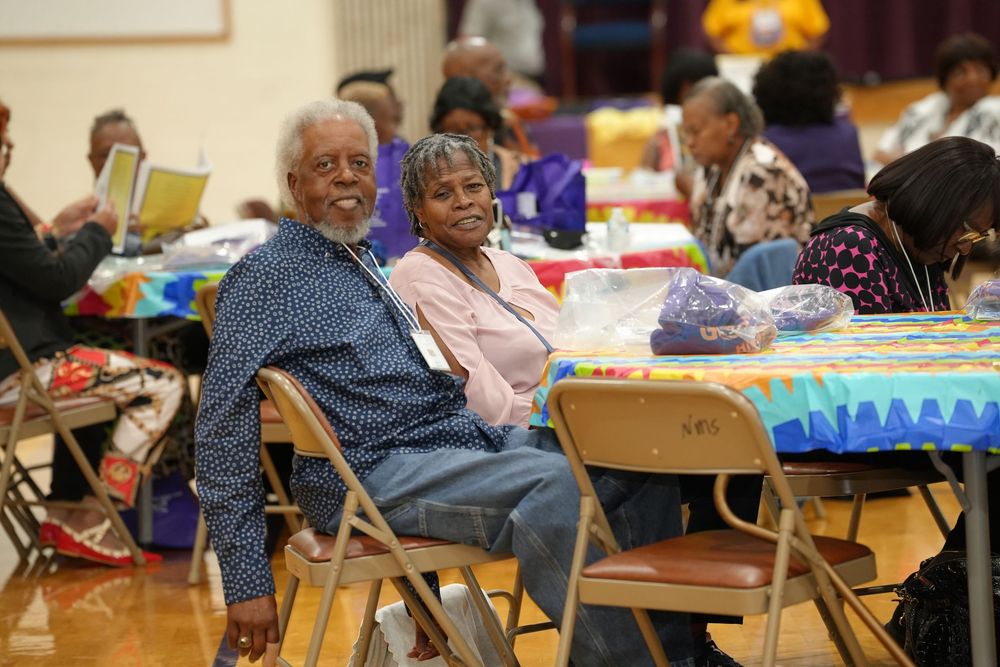 An elderly couple smiles warmly while seated at a decorated table during a community gathering event.