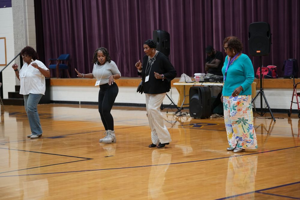 Four people dancing on gymnasium floor during lively community celebration event indoors.