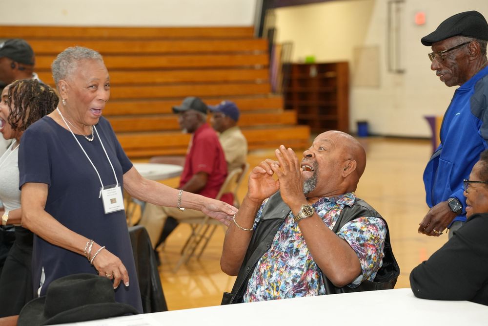 Elderly people socializing at an indoor community event, with a man laughing joyfully while seated at a table.