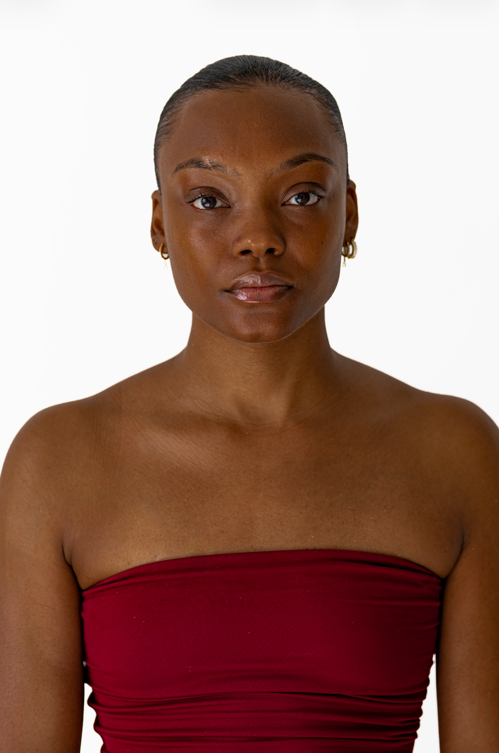 Front-facing portrait of a young Black woman in a red strapless top against a white background.