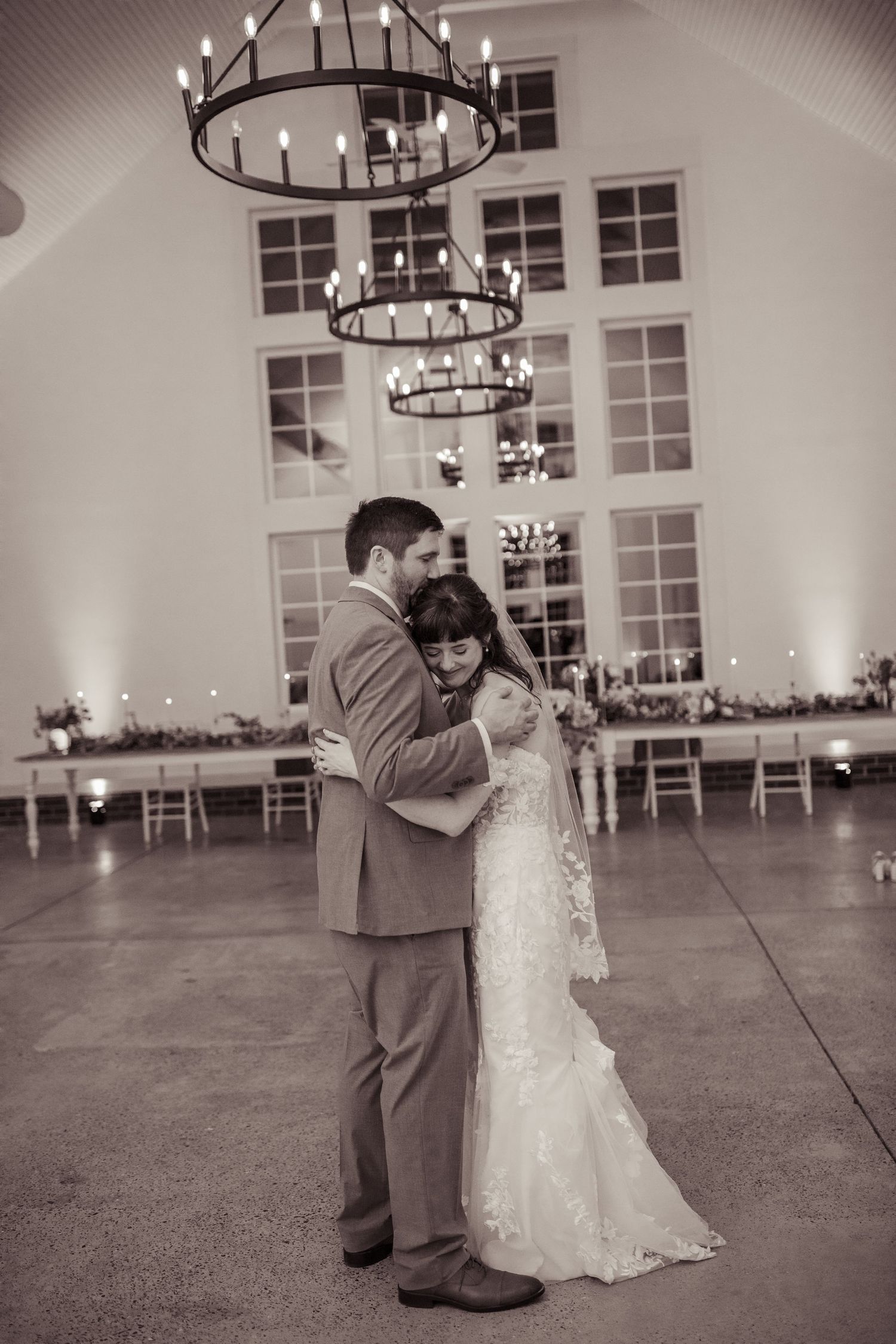 Bride and groom share first dance under candlelit chandeliers in elegant wedding venue, black and white photo.
