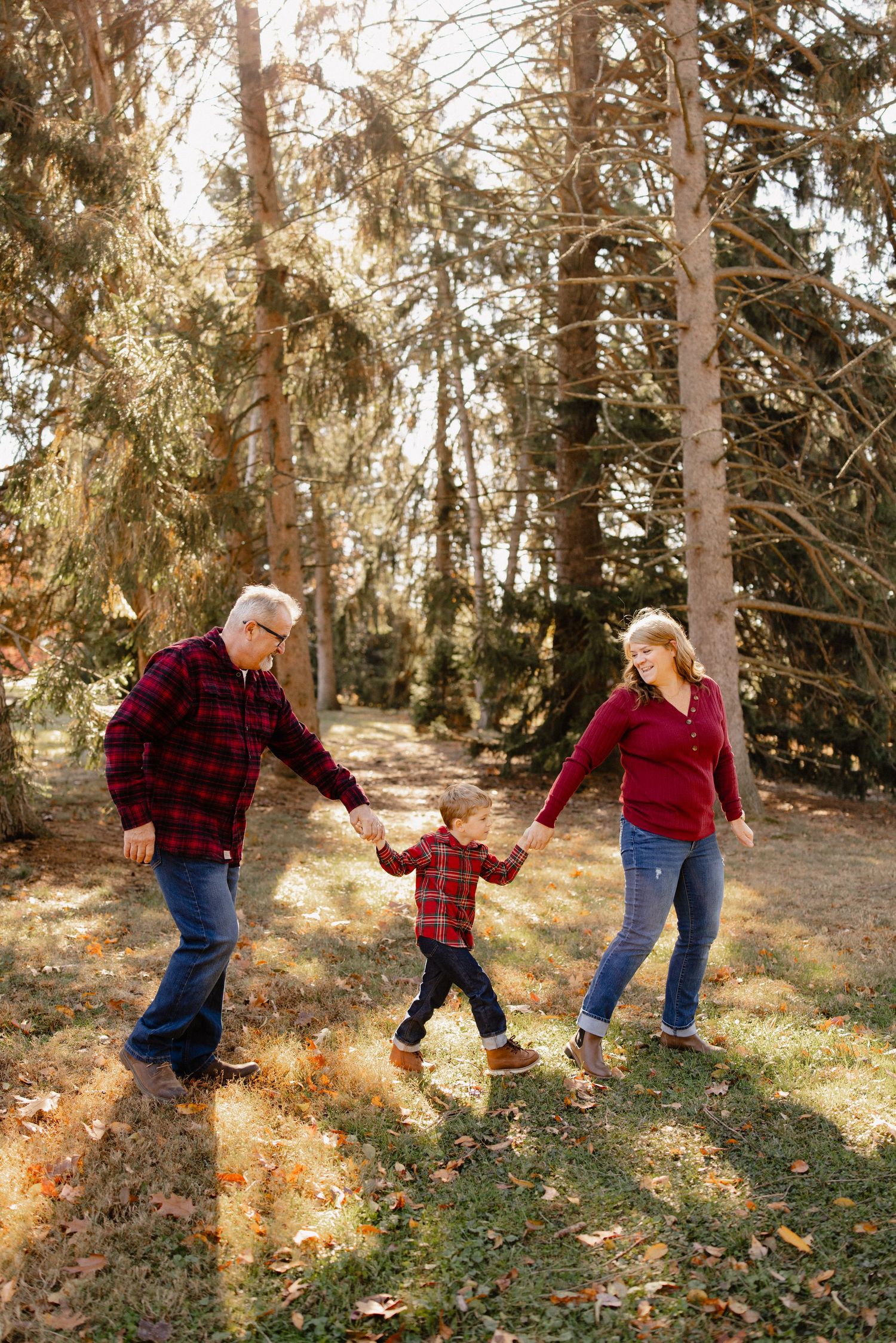 Family of three in matching red plaid holding hands walking through a sunny autumn forest park.