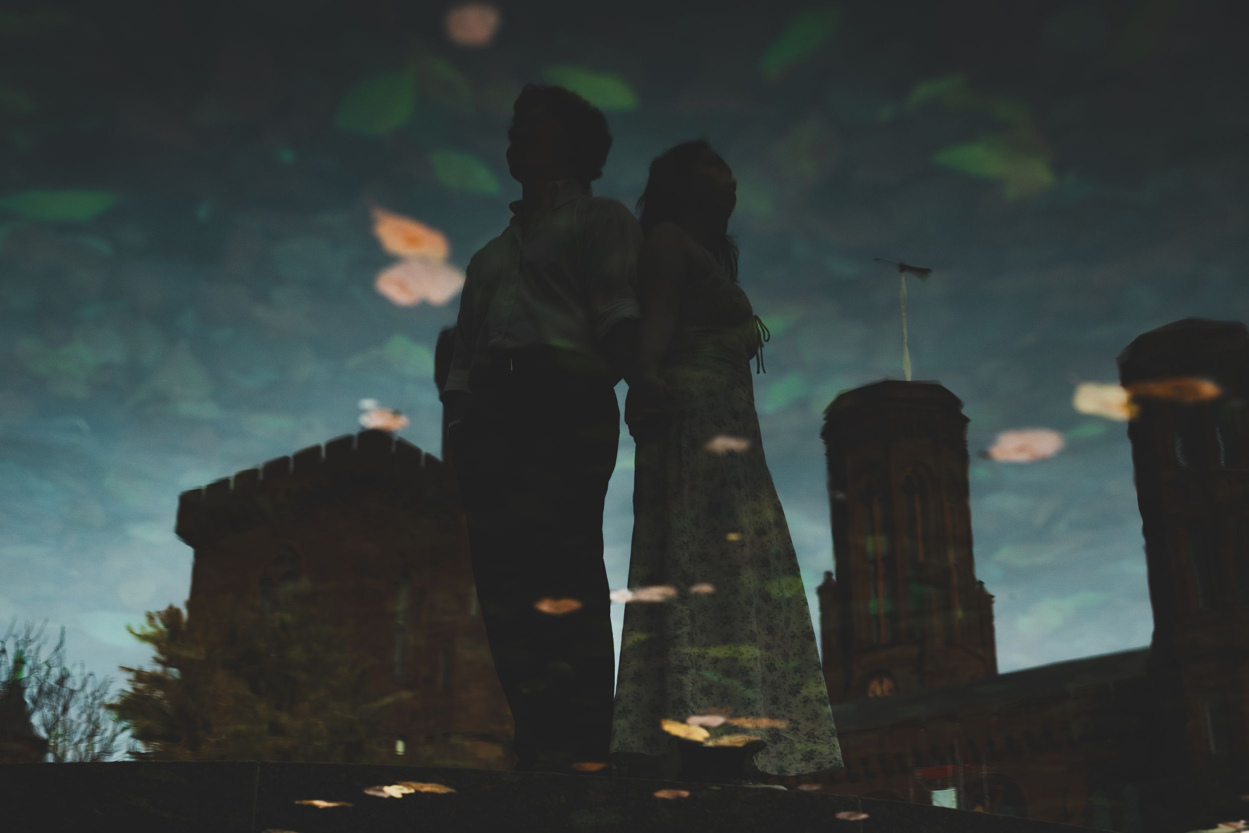 Romantic couple silhouette reflected in a puddle with castle towers and bokeh lights at dusk.