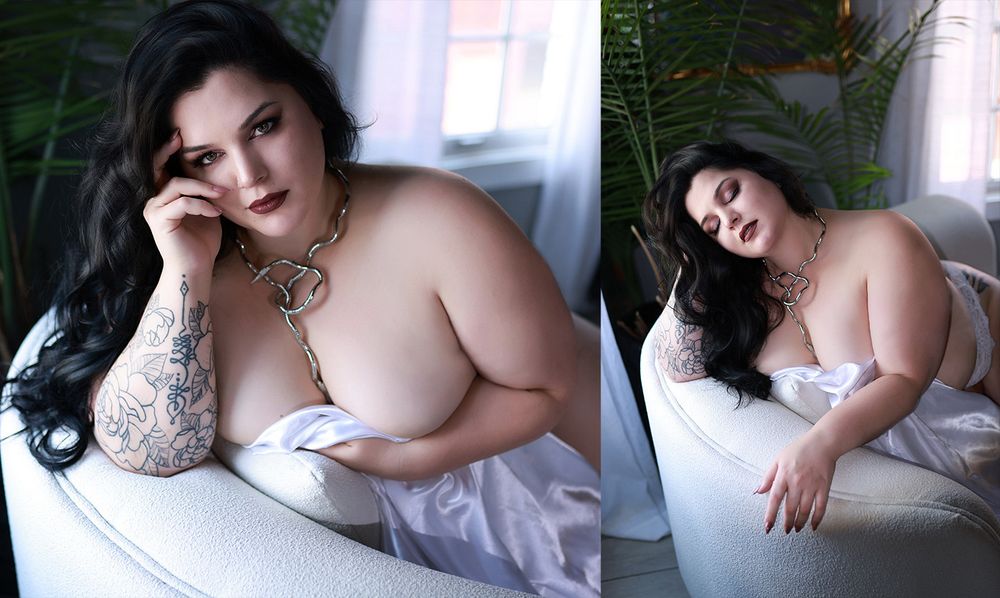 Plus-size woman with tattoos poses in white lingerie near a window in a boudoir-style photo shoot.