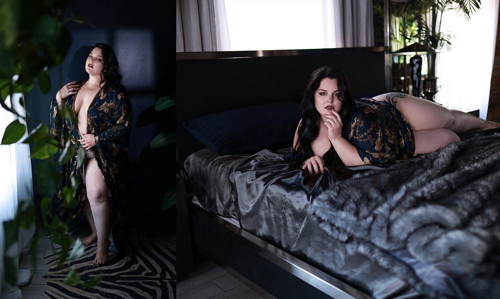 A woman in a black robe poses elegantly in a moody, plant-filled bedroom with dark satin bedding.
