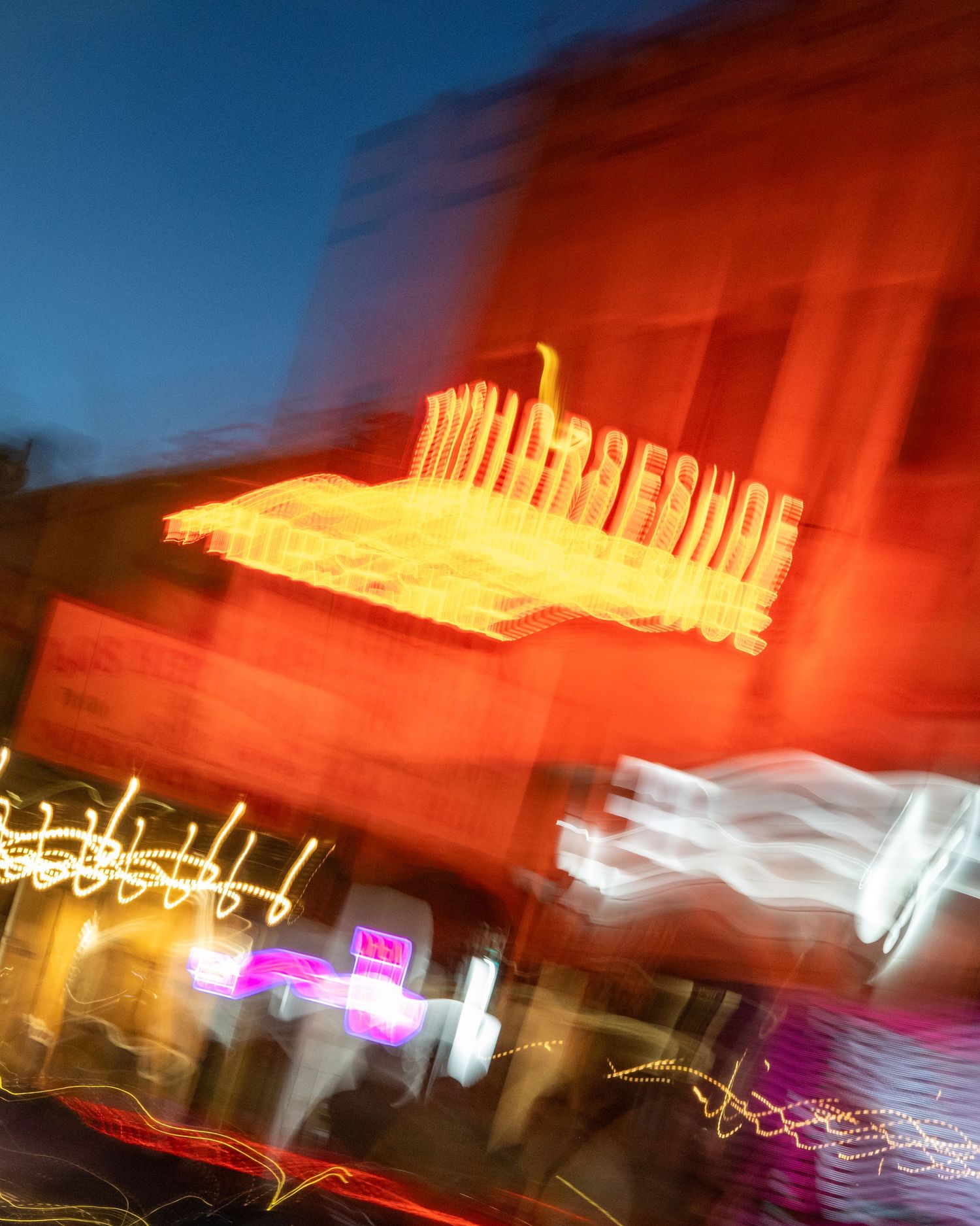 Blurred neon lights of the Horseshoe sign glow in vibrant red and orange hues against a twilight sky.
