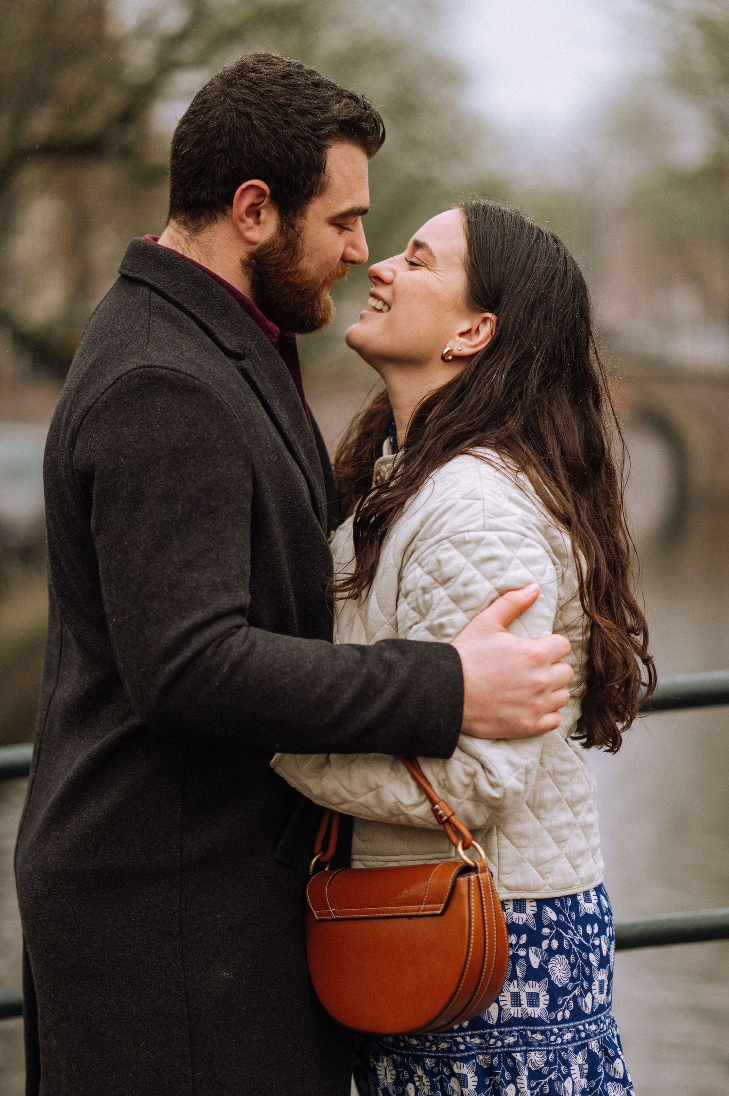 Man proposes to woman on one knee beside Amsterdam canal with bicycles and historic buildings in background.