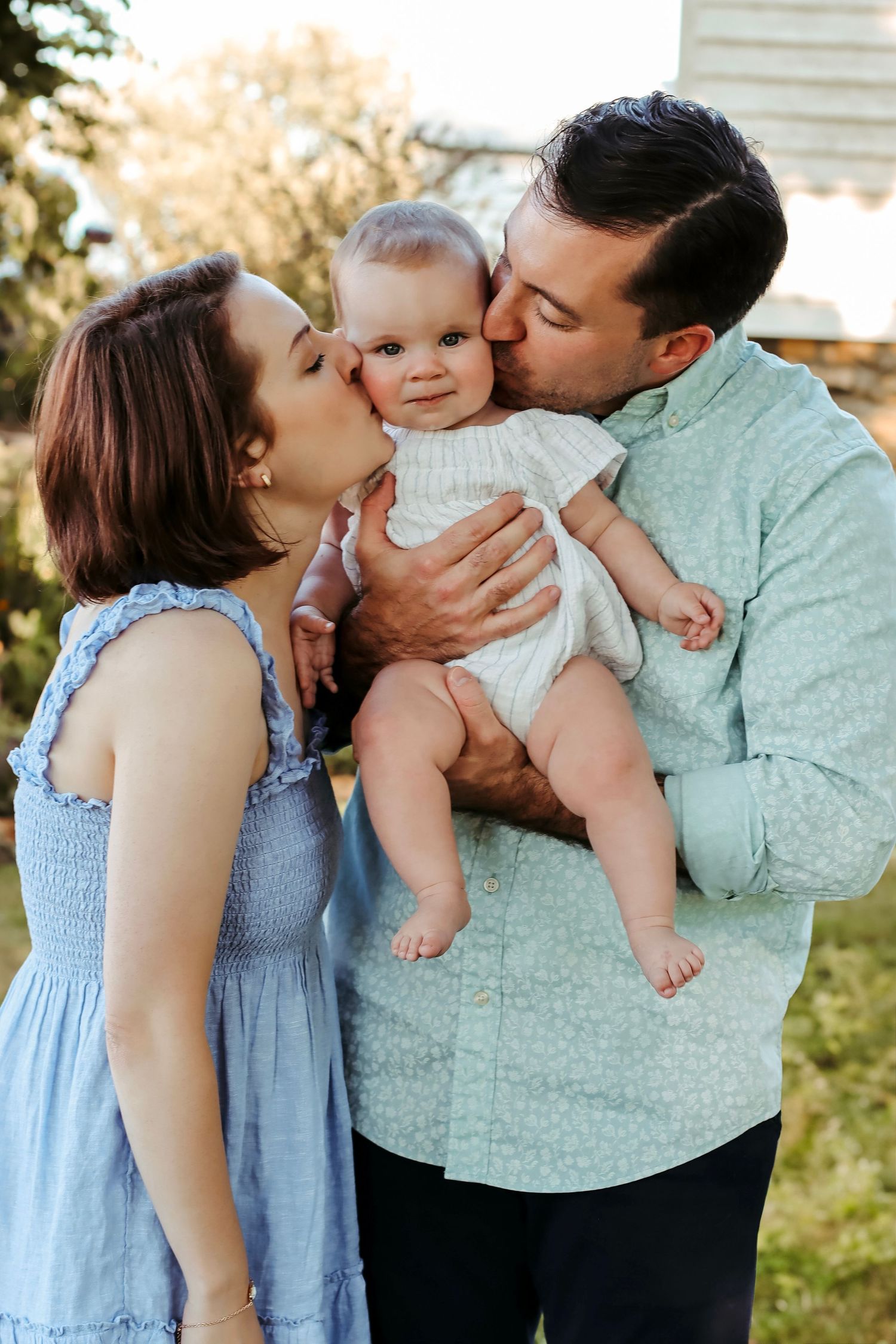 Family of three with baby and cat enjoying a picnic on a blanket in a lush green garden.