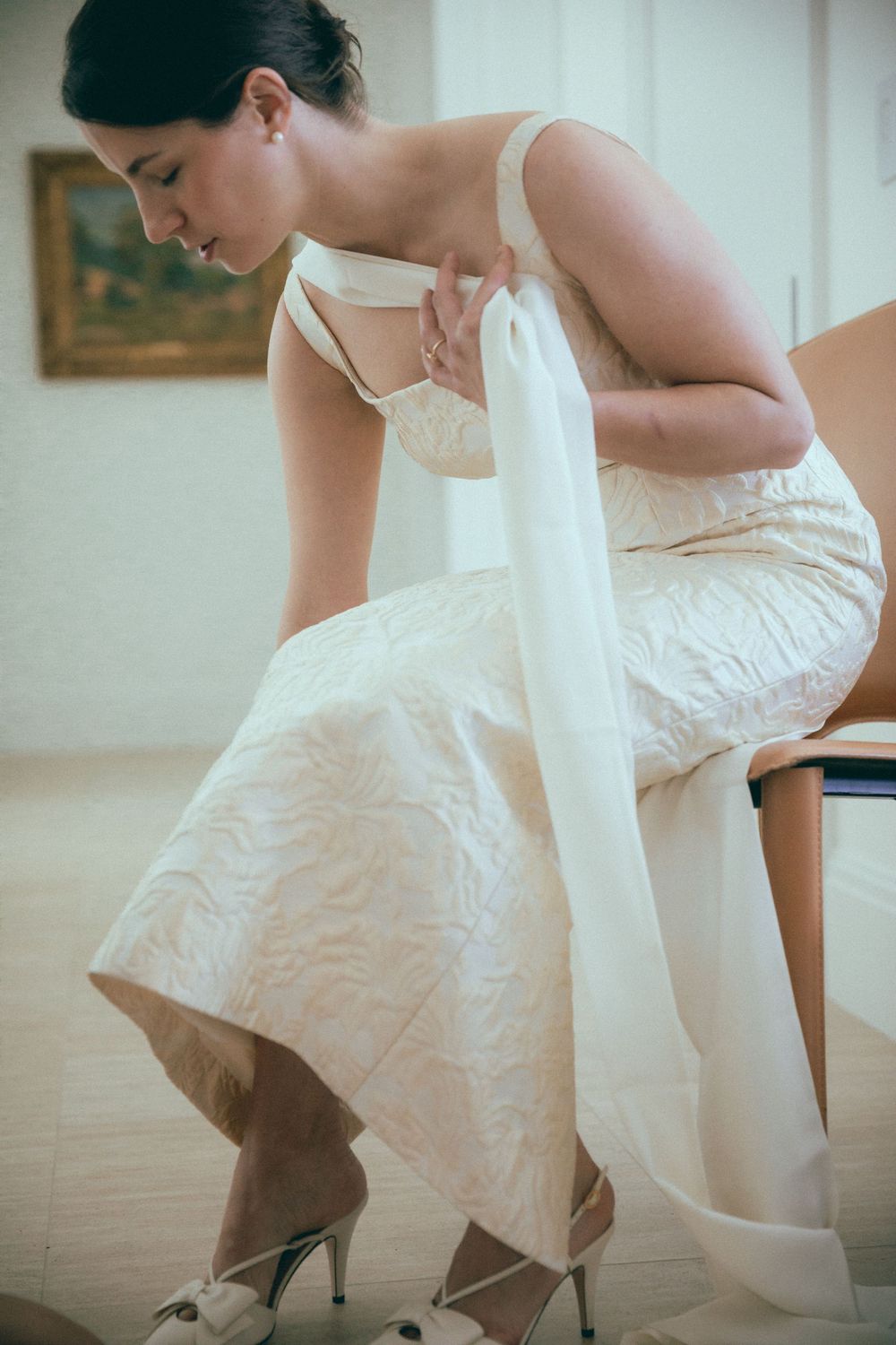 Bride in embroidered wedding dress adjusting her heel while seated, preparing for her wedding day.