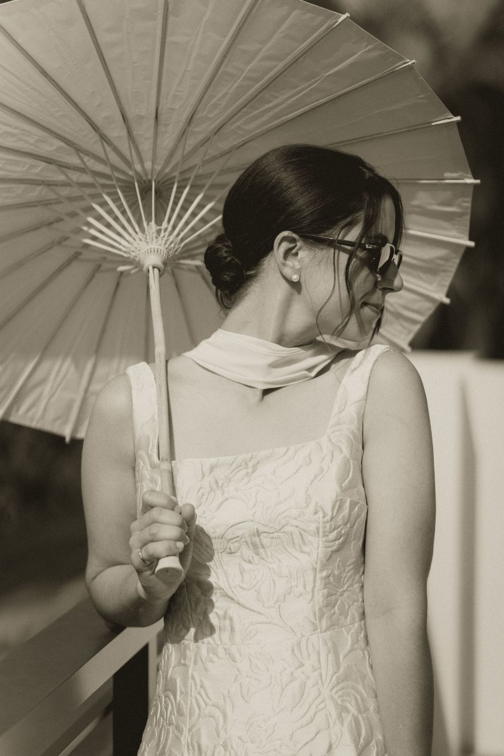 Bride in white lace dress holding a paper parasol umbrella, sepia-toned wedding portrait.