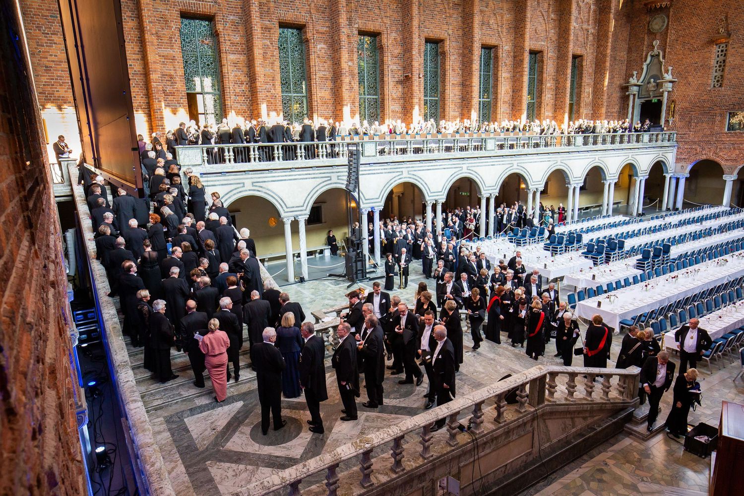 Elegant formal gathering in a grand historic hall with ornate arches, attendees in formal attire on a grand staircase.