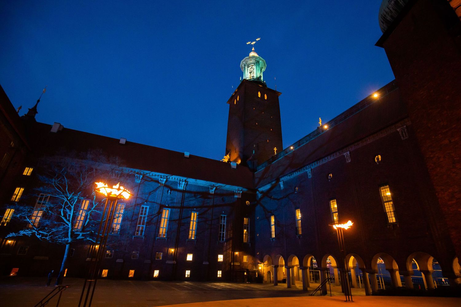 Stockholm City Hall illuminated at night with blue sky, glowing tower and warm lights in courtyard.