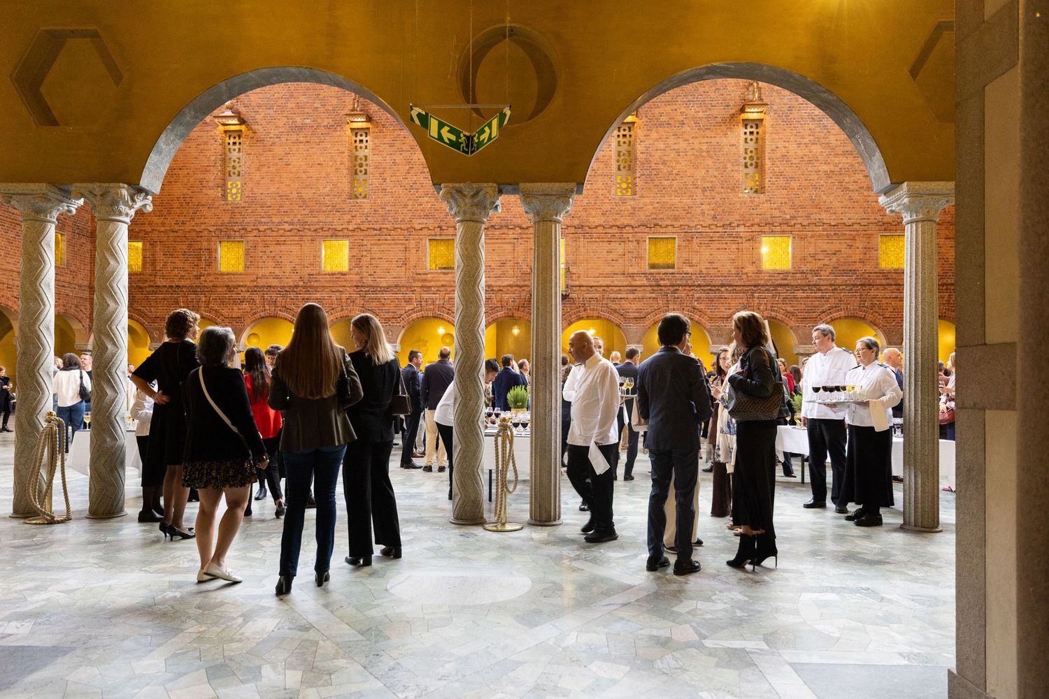 Elegant indoor courtyard event with guests mingling under arched brick walls and marble floors.