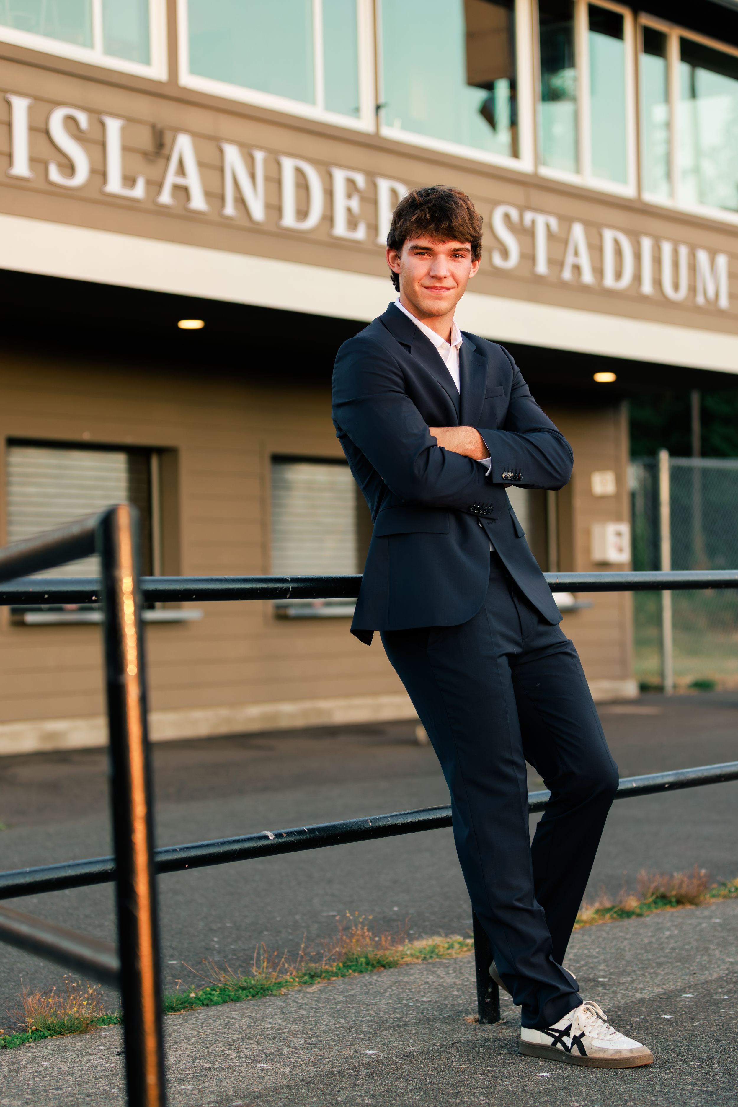 Young man in navy suit posing confidently with arms crossed outside Islander Stadium.