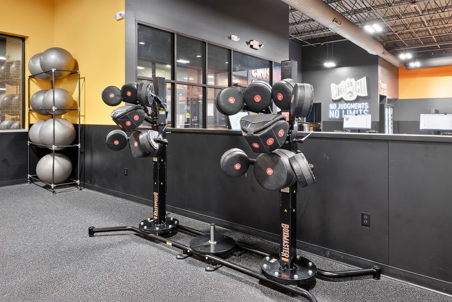 Commercial gym equipment with weight plates and medicine balls on racks in a modern fitness center with orange accents.