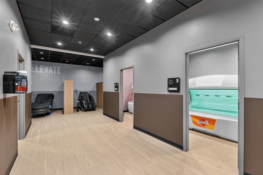 Modern gym wellness area featuring tanning beds and massage chairs in a clean, well-lit facility.