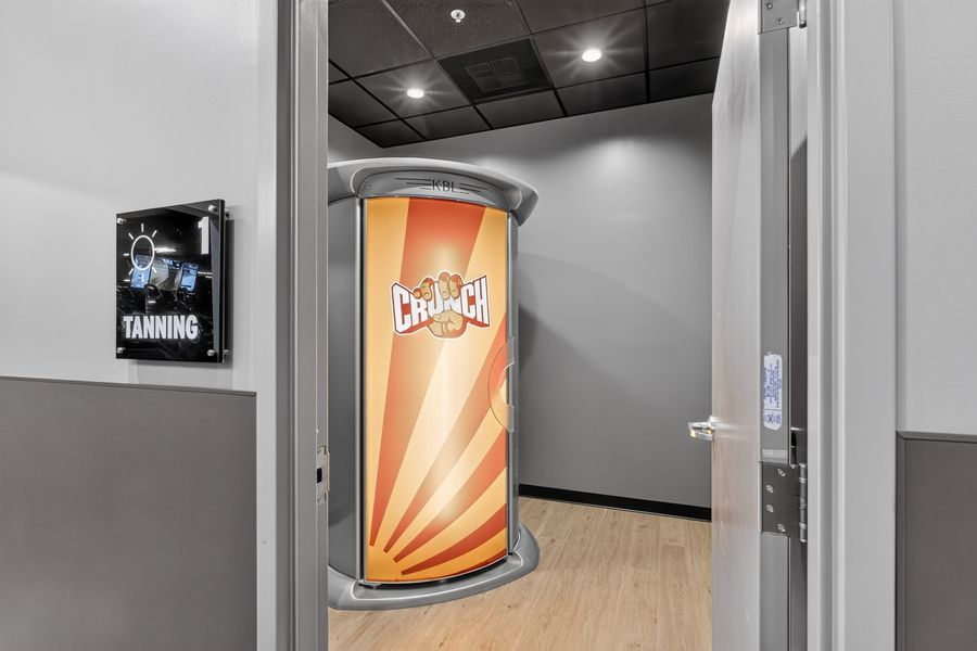 Crunch Fitness tanning room entrance featuring a cylindrical stand-up tanning booth with branded design.