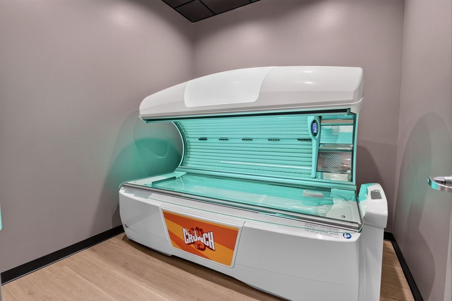 Modern tanning bed with glowing turquoise lights open and ready for use in a clean private tanning room.