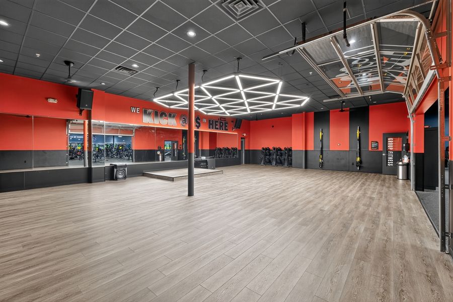 Spacious gym studio with red accent walls, wood floors, mirrored walls, and modern geometric ceiling lights.