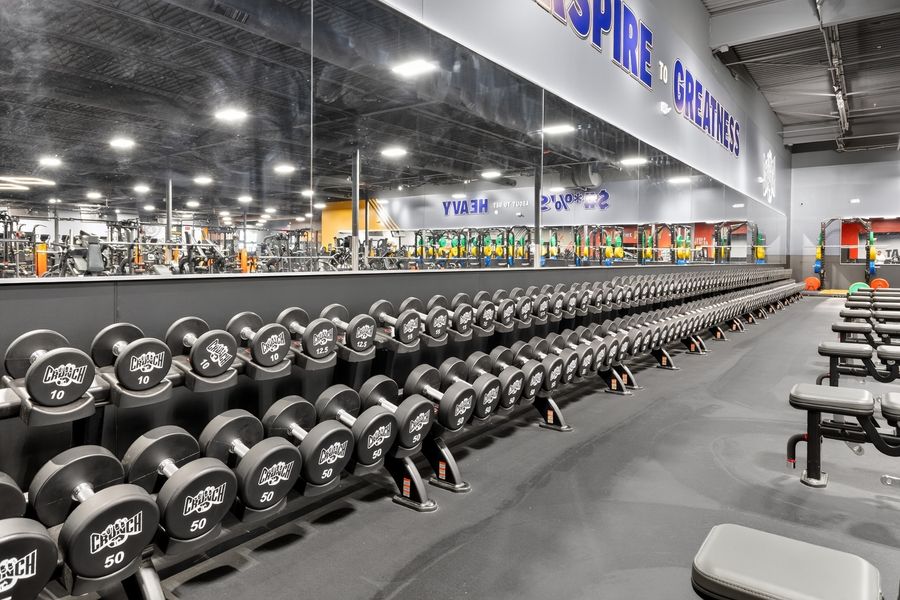 Large gym with rows of dumbbells on racks, open floor space, and motivational signage in a modern fitness center.
