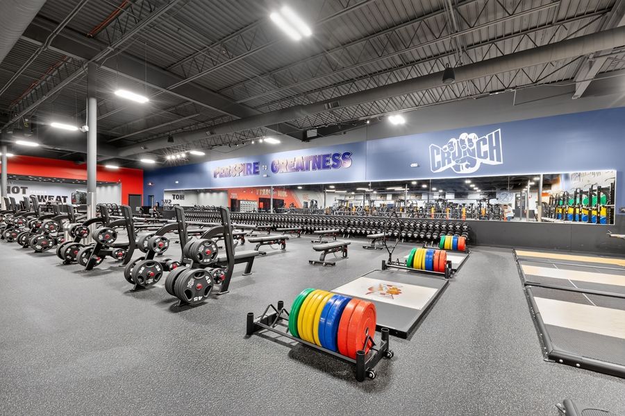 Crunch Fitness gym interior with rowing machines, colorful weight plates, and extensive free weight area on rubber flooring.