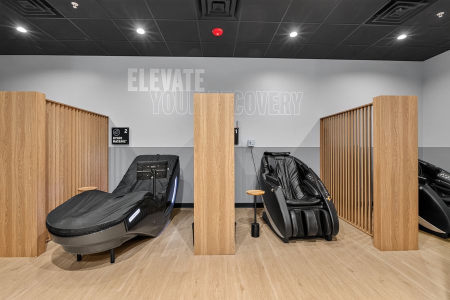 Modern gym recovery room featuring massage chairs and relaxation pods with Elevate Your Recovery signage.