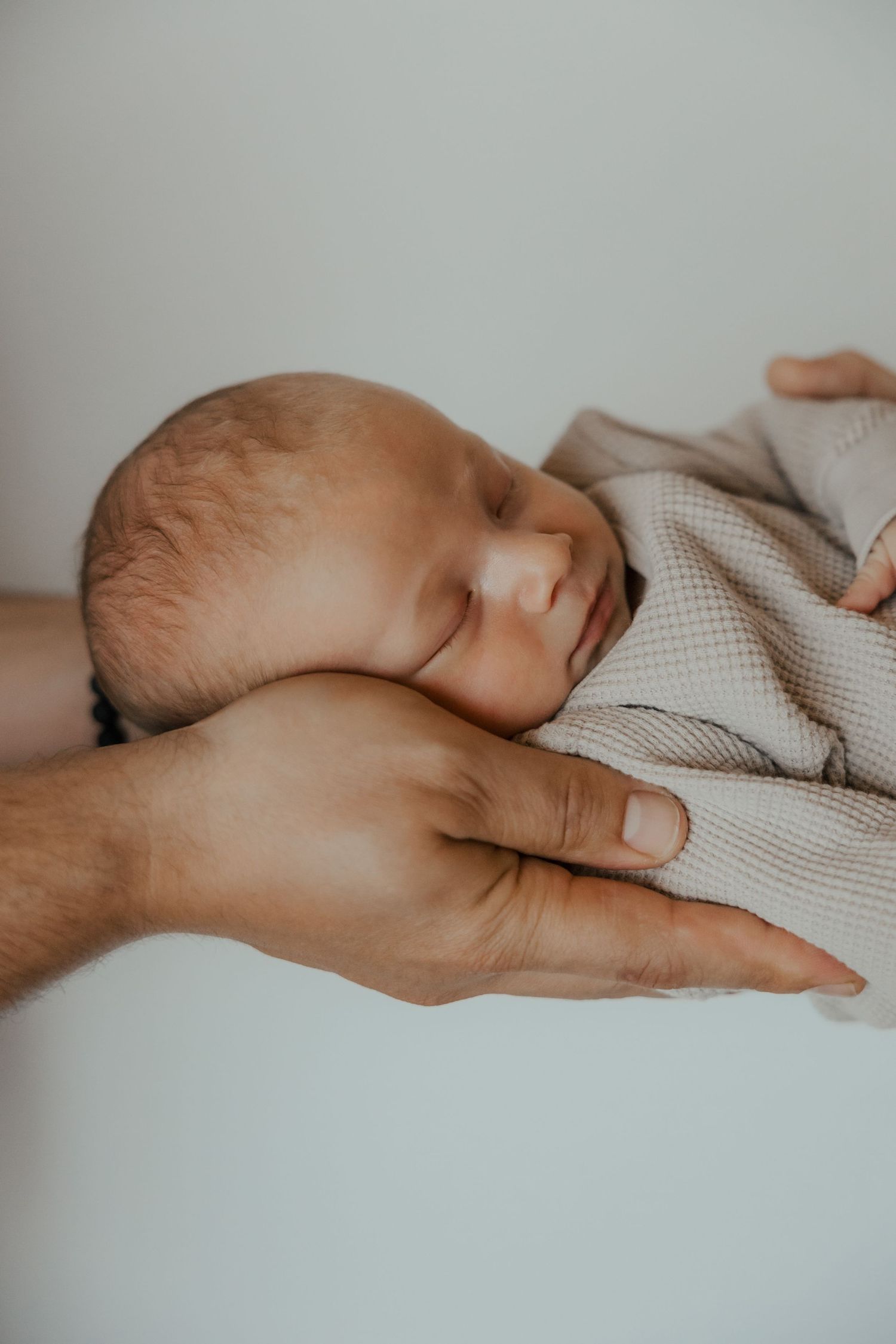 Close-up of adult hand gently touching sleeping baby's hand on textured blanket.