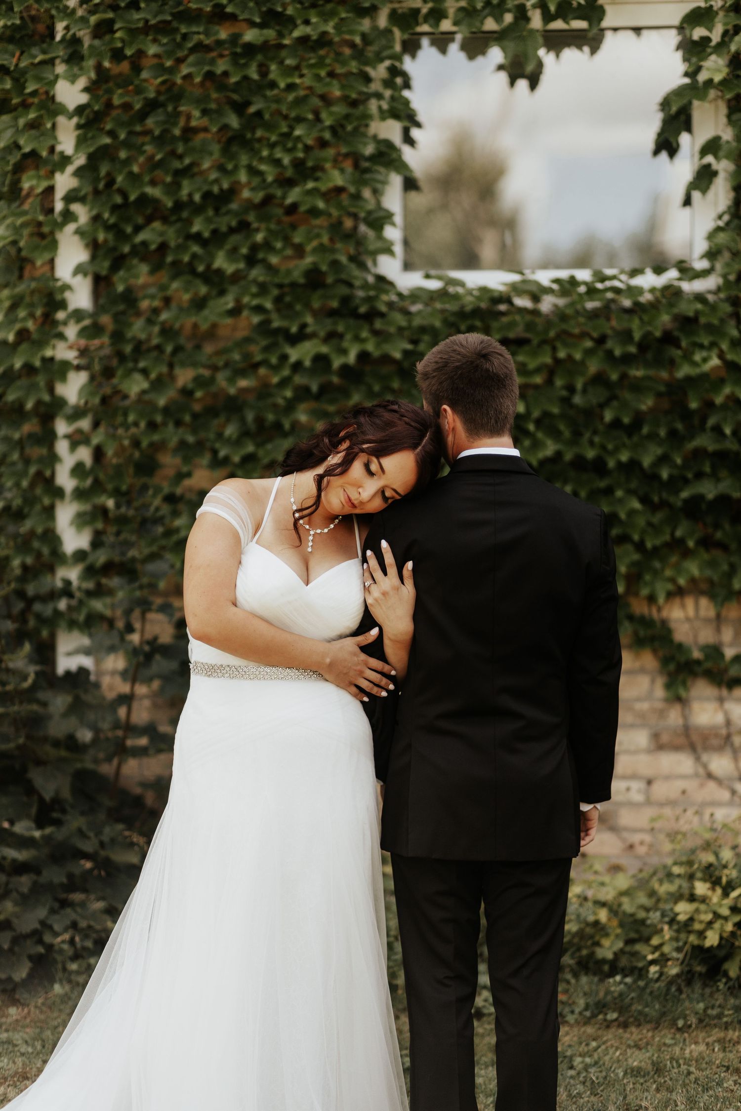 Intimate moment between couple against ivy-covered wall.