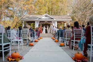 Outdoor wedding ceremony venue decorated with white chairs, autumn pumpkins, and fall foliage.