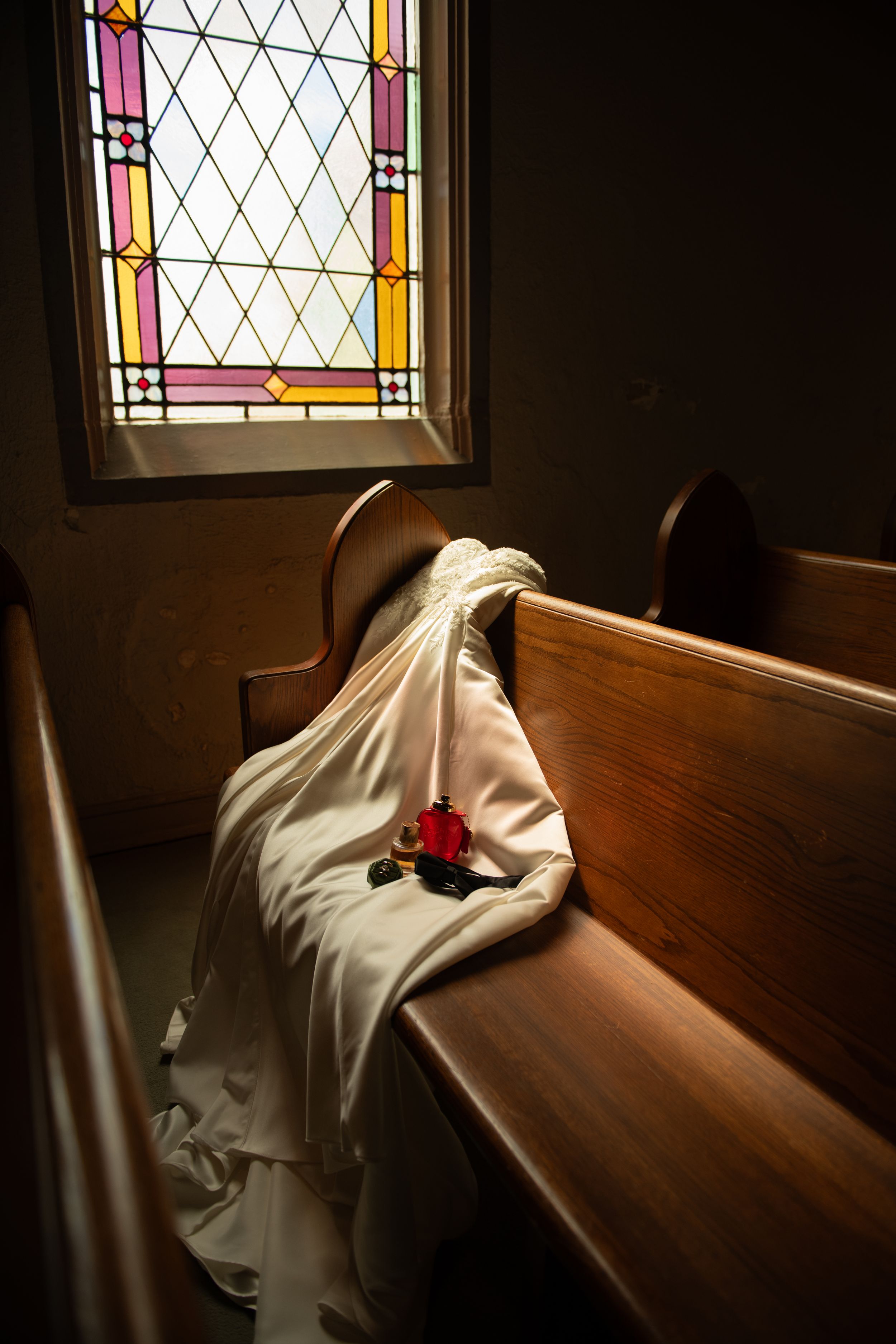 Dramatic lighting through stained glass windows illuminates wooden church pews.