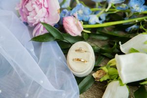 Wedding rings displayed on white tulle fabric with pink and white flowers.