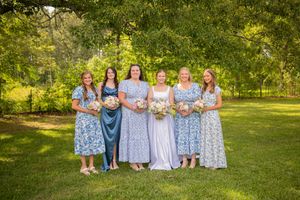 Wedding party in light blue dresses posed outdoors in a garden setting.