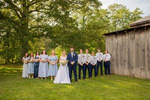 Wedding party lined up for formal portraits in front of rustic barn and trees.
