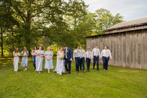 Panoramic shot of wedding party arranged in front of rustic barn during autumn.