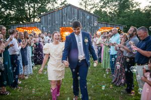 Outdoor wedding celebration with rustic barn backdrop and string lights at dusk.