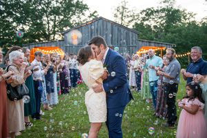 Wedding celebration scene with guests gathered outside a rustic barn under string lights.